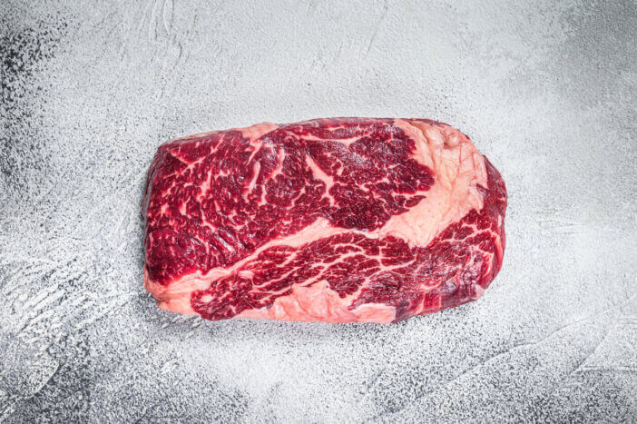 Raw rib eye beef meat steak on a table prepared for the gril. White background. Top view
