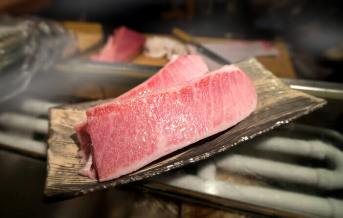 cutting of otoro from blue fin tuna for sashimi at the kitchen bar of sushi restaurant photo with indoor very low and dark lighting.