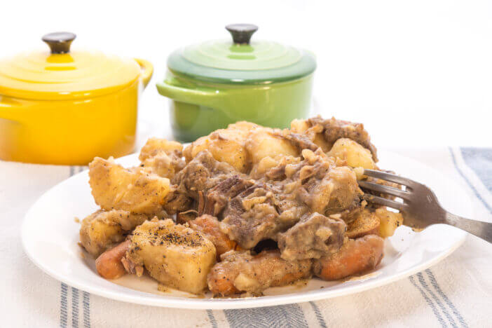 Plate of venison stew  on old kitchen dish cloth with white background.