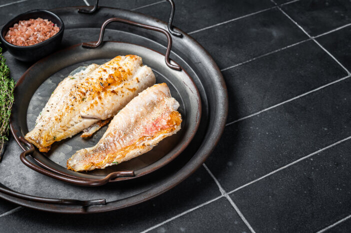 Roasted ocean red perch fillet with olive oil, thyme and spices. Black background. Top view. Copy space.