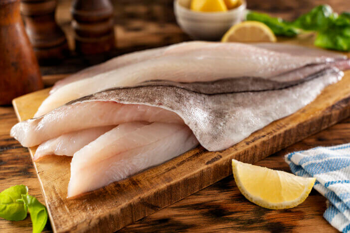 Fresh haddock fillets on a rustic cutting board with lemon and herbs.