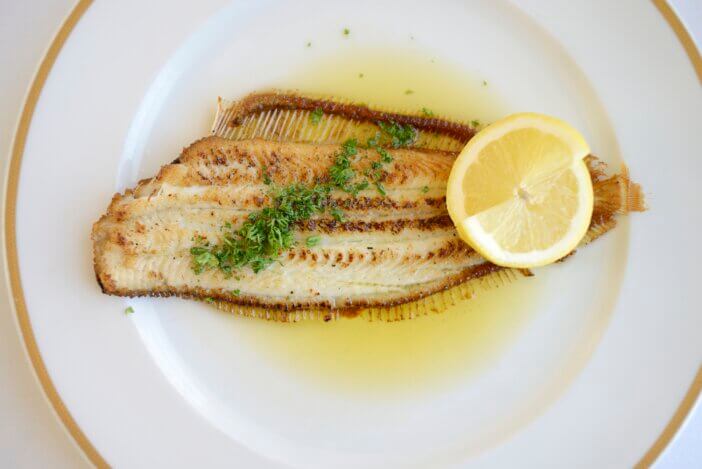 "A delicious serving of locally caught Sole Meuniere with fresh lemon on a white plate, in a restaurant."