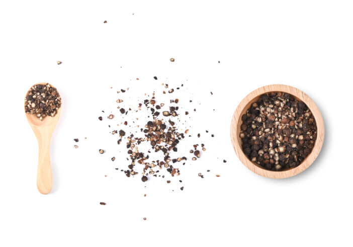 Coarsely crushed ground black pepper in wooden spoon and wooden bowl isolated on a white background. Top view