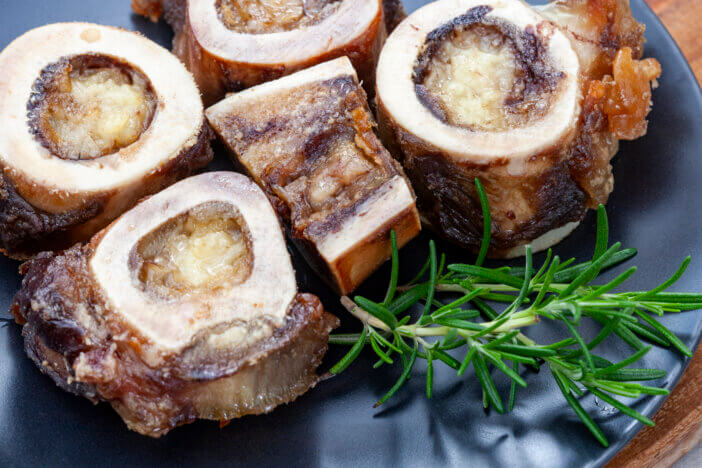 Roasted Marrow bones on a black plate with rosemary garnish