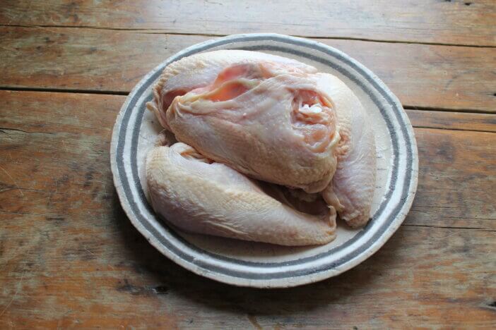 Four Split Chicken Breasts on a plate sitting on a distressed wooden table. The chicken is bone-in, skin on in natural light.