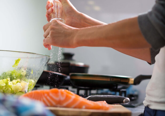 Young woman seasoning a salmon filet in her modern kitchen, prepaaring a healthy food