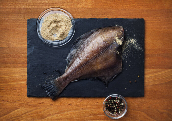 Flounder fish with spices, pepper, salt and slate cutting board on wooden background. Flat lay.