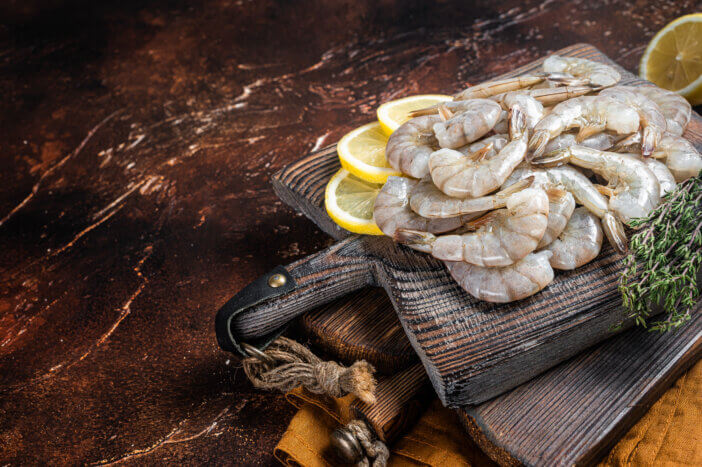 Raw tiger white shrimp prawn on board with herbs. Dark background. Top view. Copy space.