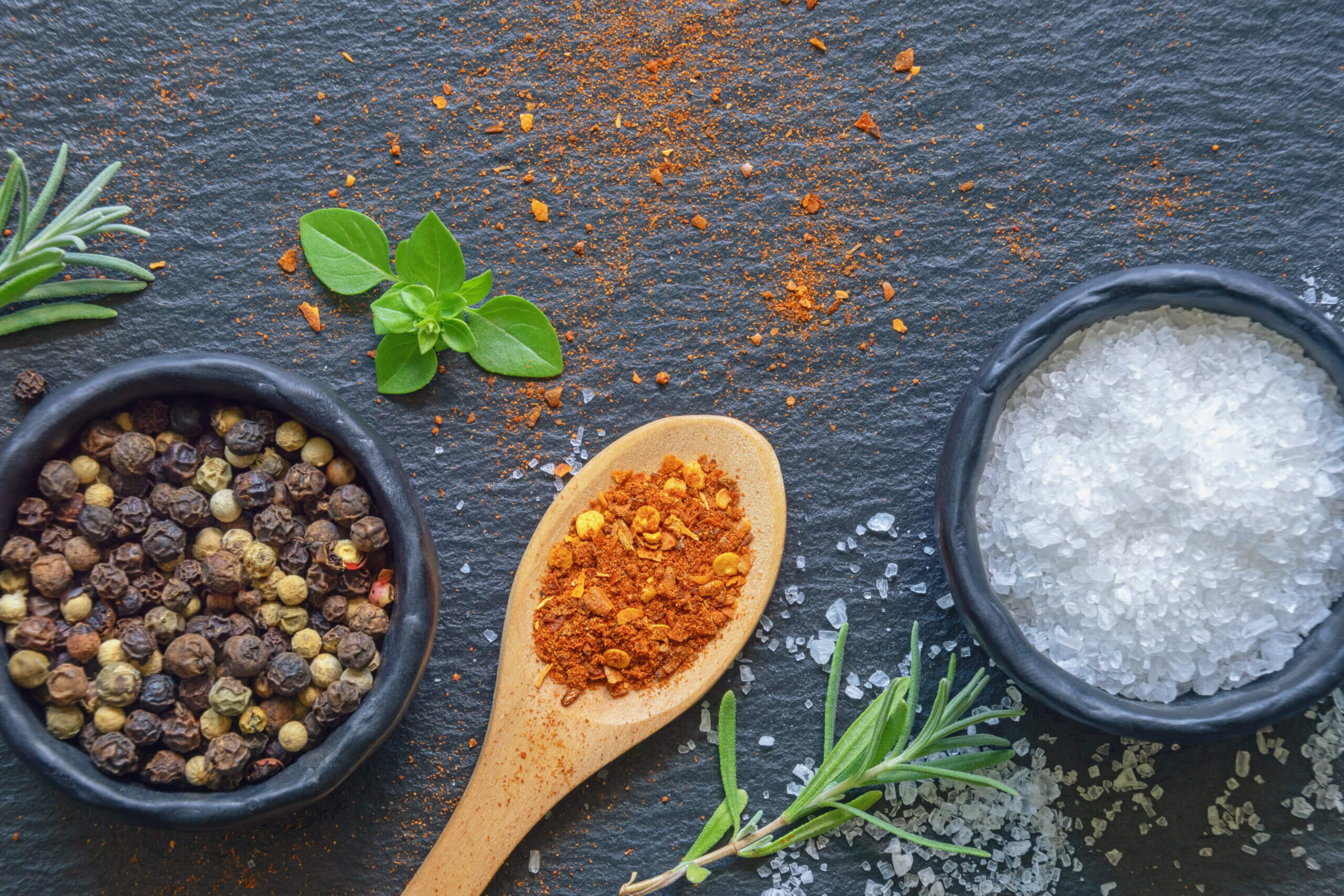 Salt and pepper. Sea salt and peppercorns in  small black dishes. Paprika in wooden spoon. Flat lay, black background