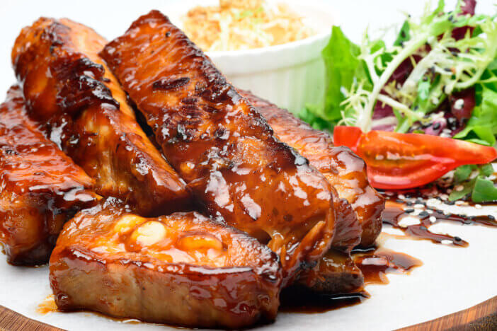 Fried pork ribs on a wooden plate decorated with salad