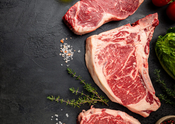 Variety of Fresh Raw Black Angus Prime Meat Steaks T-bone, New York, Ribeye and seasoning on black background, top view