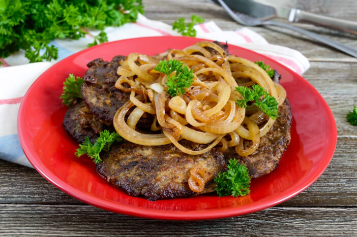 Juicy slices of fried liver and onions on a red plate.