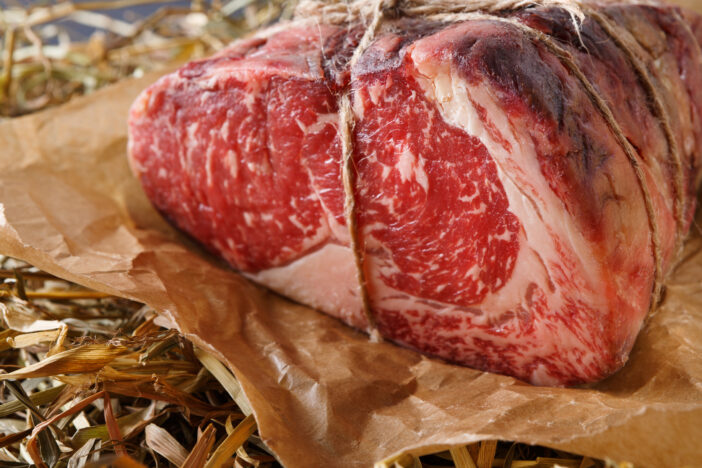 Raw black angus beef bound with rope in craft paper on straw. Aged prime marble meat closeup