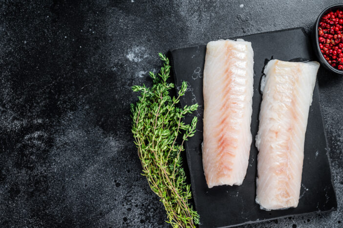 Raw cod loin fillet fish on marble board. Black background. Top view. Copy space.