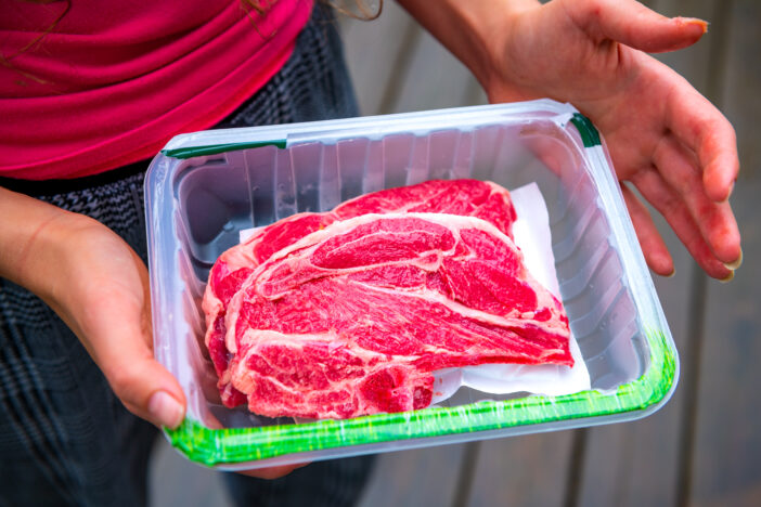 Red raw lamb meat shoulder chops from New Zealand packaged storebought with woman holding open plastic container showing