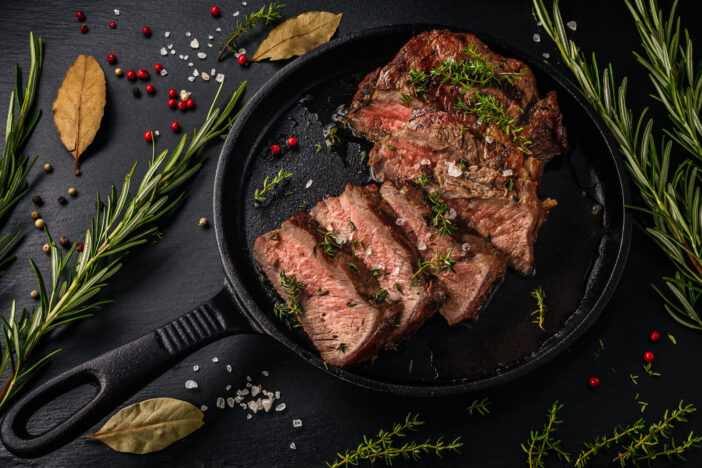 Tender sliced sous-vide beef steak in a cast iron pan on slate board. Top view