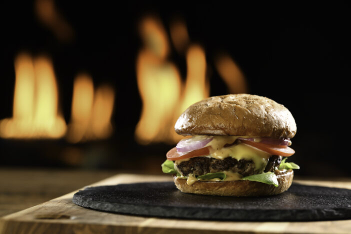 Meat cheeseburger with vegetables on black plate with flaming background.