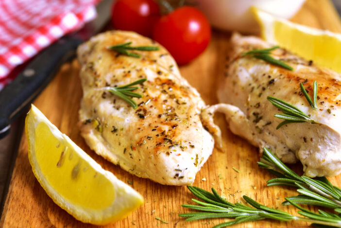 Chicken breast baked with rosemary on a cuuting board.