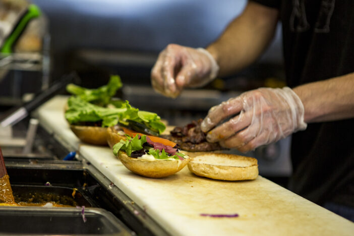 A chef adding toppings to the freshly cooked hamburgers his is preparing.