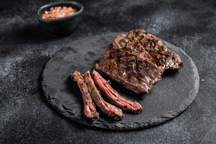 Traditional barbecue skirt steak sliced on a cutting board.  Black background. Top view.