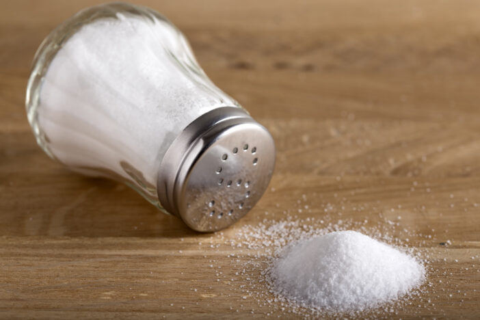 Traditional glass salt cellar and spilled salt on a wood background