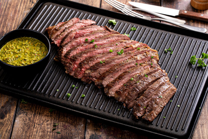 Grilled flank steak with chimichurri sauce on a grill pan on wooden table