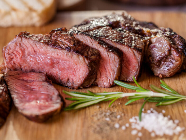 Grilled pork steak pieces with a sprig of rosemary, pepper and salt, fried pieces of bread on a wooden board. Horizontal orientation