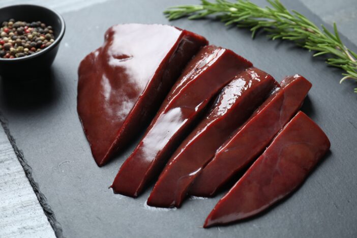 Cut raw beef liver on black table, closeup