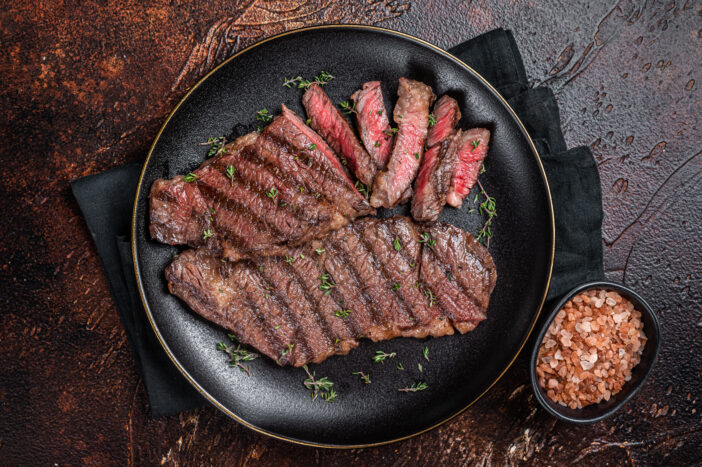 Barbecue denver strip beef meat steak on a plate. Dark background. Top view.