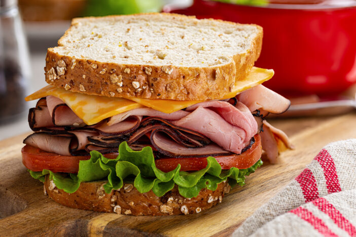 Ham sandwich with cheese, tomato and lettuce on whole grain bread on a wooden cutting board