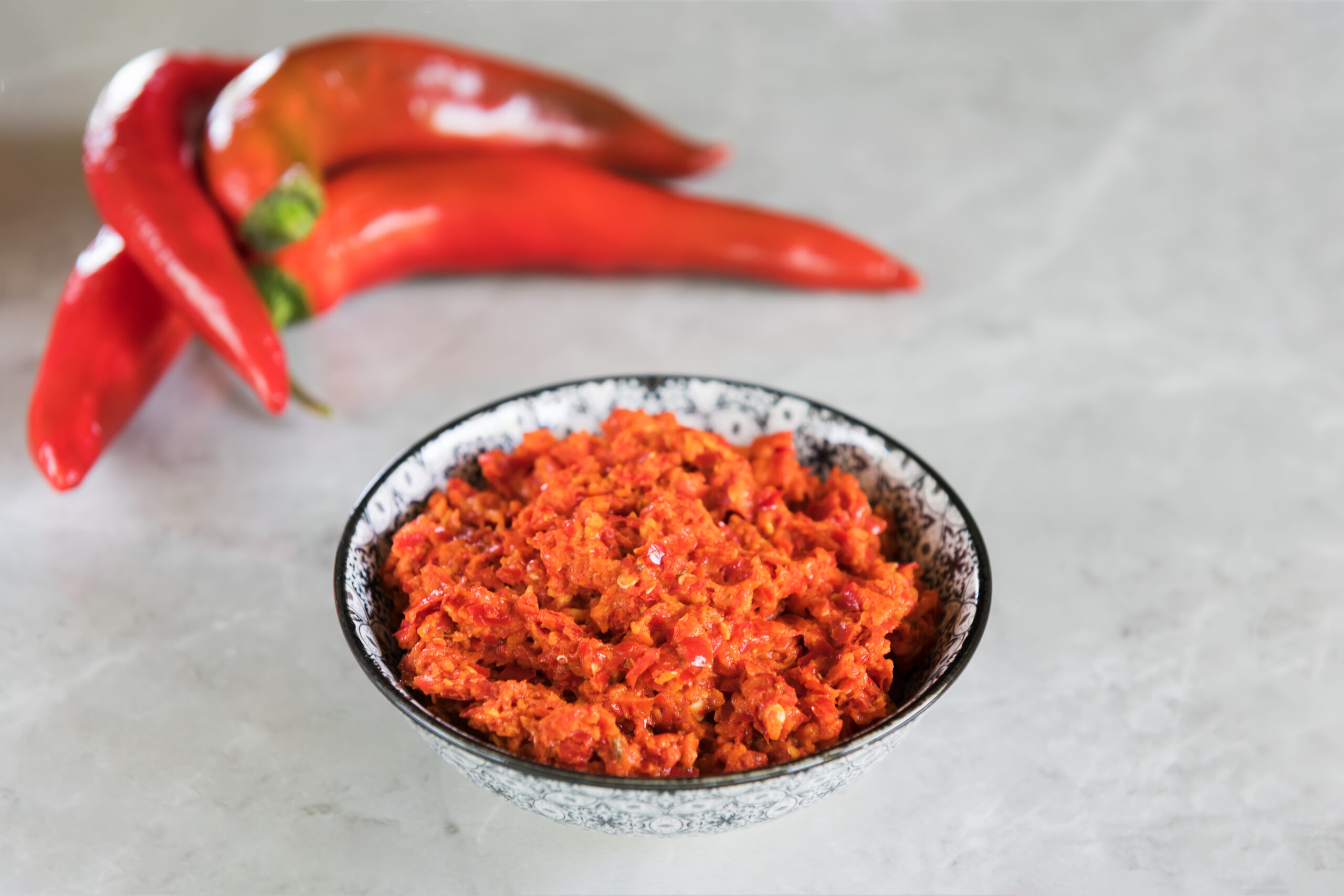 Traditional Maghrebi hot chili pepper sauce harissa on a grey marble background. Arabic cuisine. Adjika Hot Pepper Sauce. Peperoncini calabrese with olive oil, close up