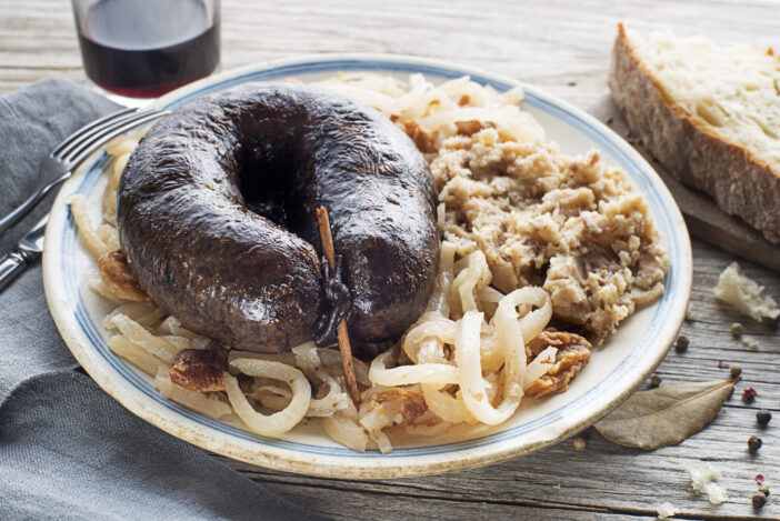 Bloody sausage morcilla, stewed sour turnip and mashed potato with brown beans close up. Traditional Slovenian dish with roasted bloody sausage