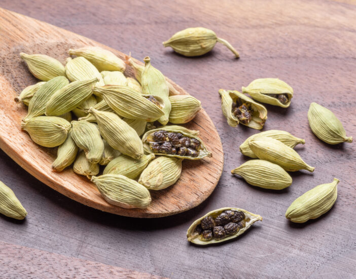 Seeds of cardamom spices in wooden spoon on a wooden table, mulled wine ingredient, macro image. Great spices background for your projects.