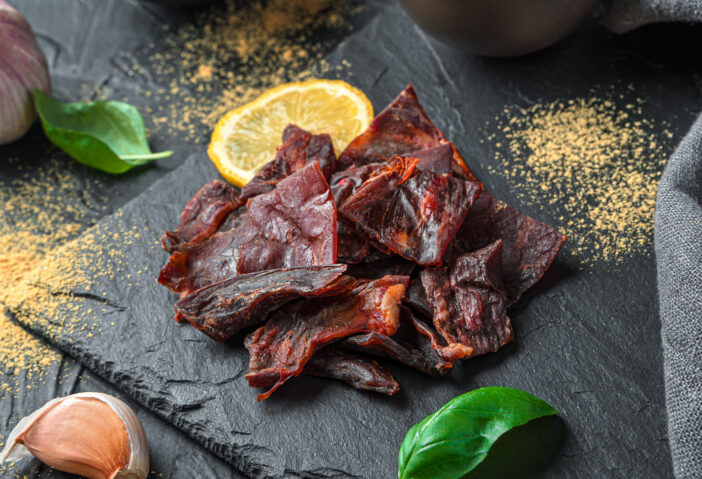 Beef jerky on a black background with spices and lemon. Side view, close-up.