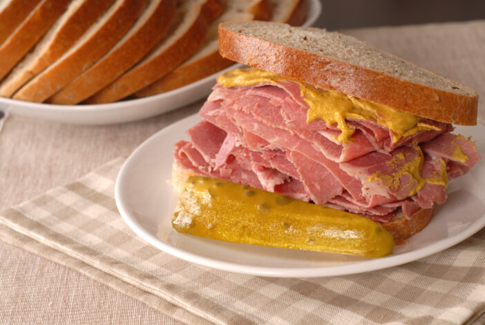 A corned beef sandwich with mustard and pickle on rye bread