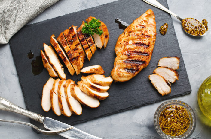 Grilled chicken fillets on slate plate. Gray concrete background