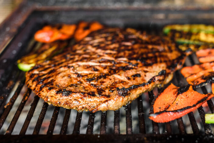 Grilling marinated angus beef flank steak on hot coals barbecue grill. Preparing juicy medium rare meat on hot grill BBQ with grill marks in restaurant fireplace.