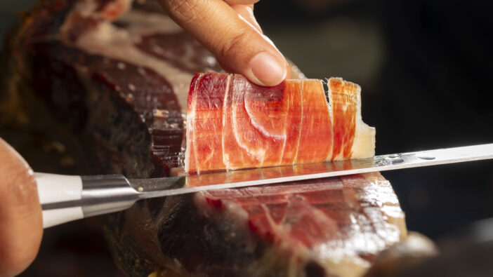 Iberian Ham. Acorn fed Iberico ham. Spanish ham 5j. Perfect slice of Iberian ham cut with a knife by a professional ready to eat. selective focus and blur background