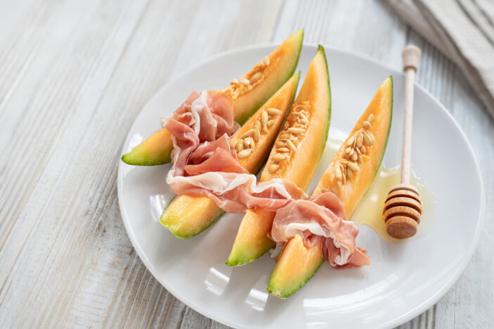 Sliced melon with prosciutto and honey; fruit and meat salad; Mediterranean sweet and savory appetizer on a plate