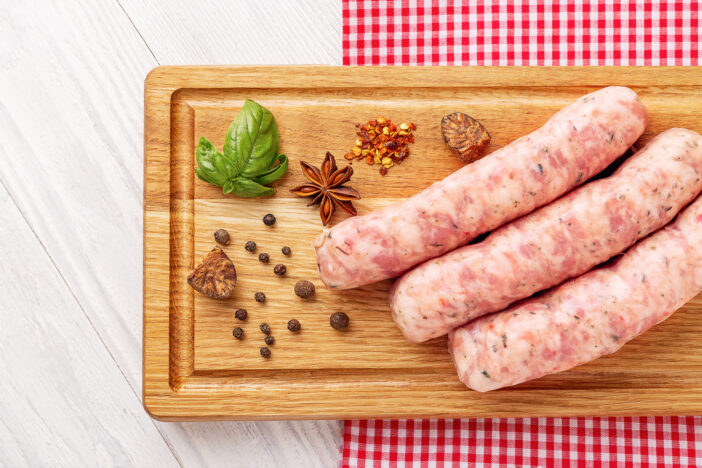 Raw sausages and spices on wooden background