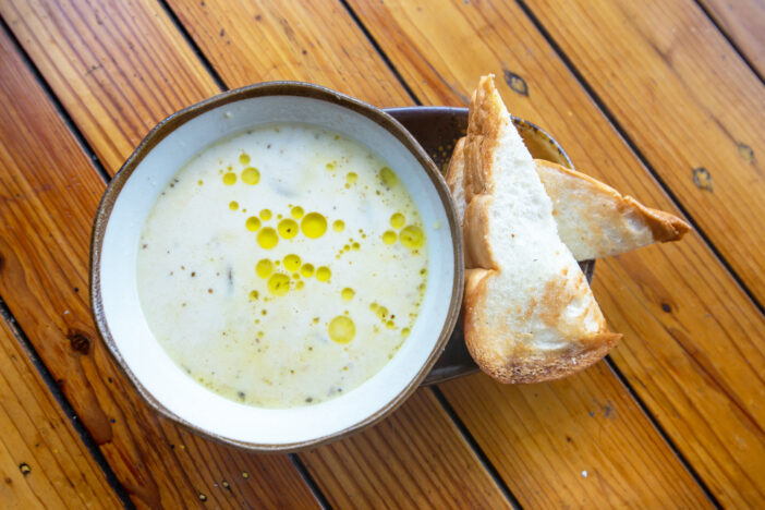 Mushroom soup bowl finished with truffle oil and toasted bread on wood background.