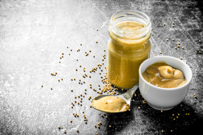 Mustard in a glass jar, spoon and bowl. On dark rustic background