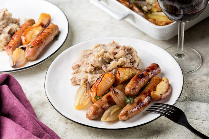 Dinner. Oven baked turkey sausages with apples and shallot onions with mashed potatoes and beans. Red wine glass.