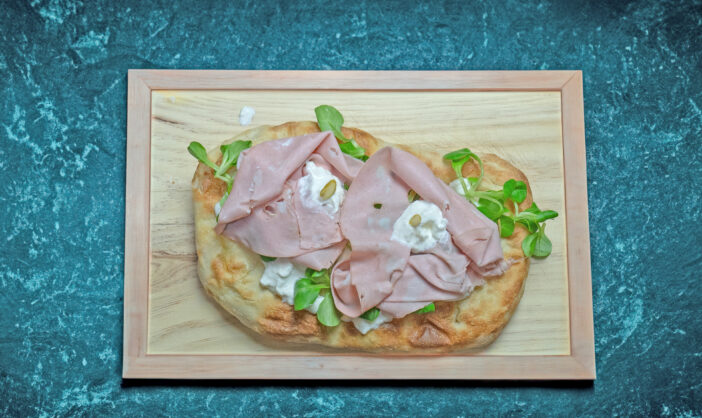 Roman pinsa, variant of the classic Italian pizza topped with mortadella, stracciatella and lamb's lettuce and pistachios