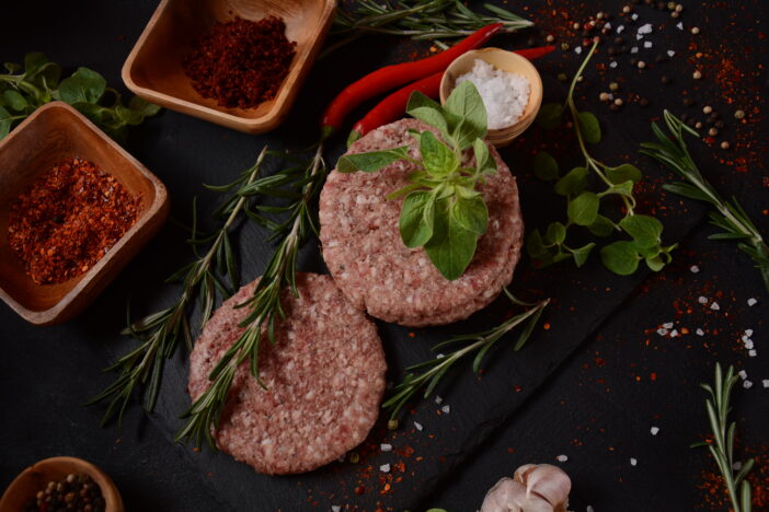 Raw beef hamburger patties with herbs and spices. Raw burger cutlets on a concrete background