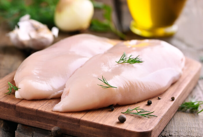 Raw chicken breasts and spices on wooden cutting board, close up view