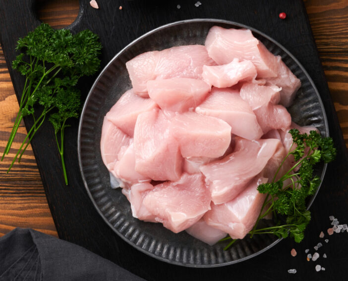 Raw chicken breast sliced or cut pieces on wooden cutting board with herbs and spices on old wooden table background. Raw chicken meat. Top view with copy space. Mock up.