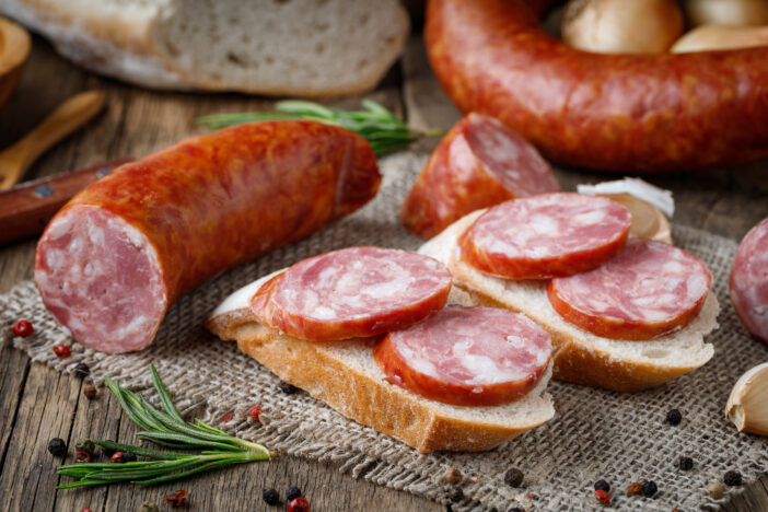 Sandwich with smoked sausage. Dry-cured sausage, bread and spices on a wooden table.