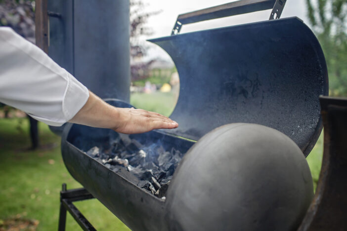 Smoker grill in home backyard, container with coal, smoke coming out of a smokestack, barbecue on green background, family patio, outdoor bbq party on open air