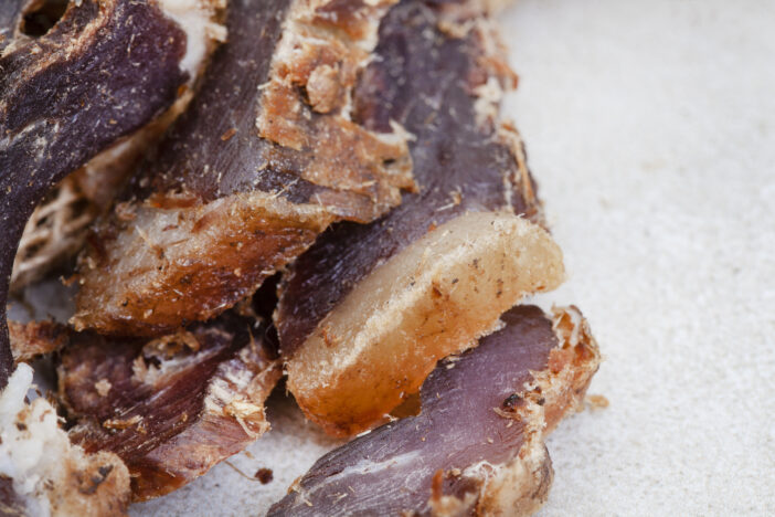 South African Biltong, a dried and cured meat sliced and on grey backdrop with copy space